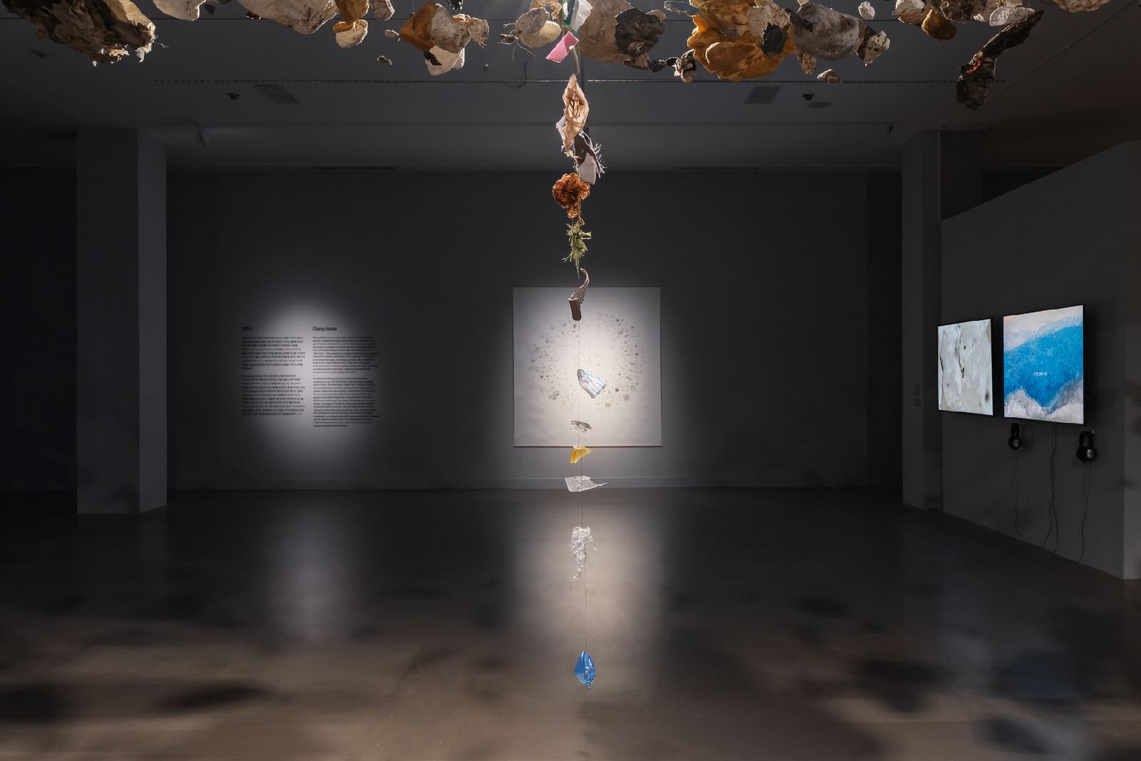 Detail of Being: a suspended column of plastic descending toward a spread of New Rocks