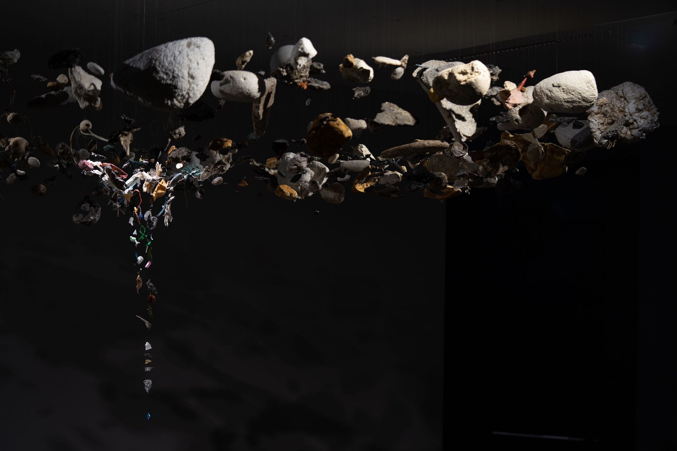 Being, 2025: hundreds of weathered plastic fragments suspended in a darkened museum hall