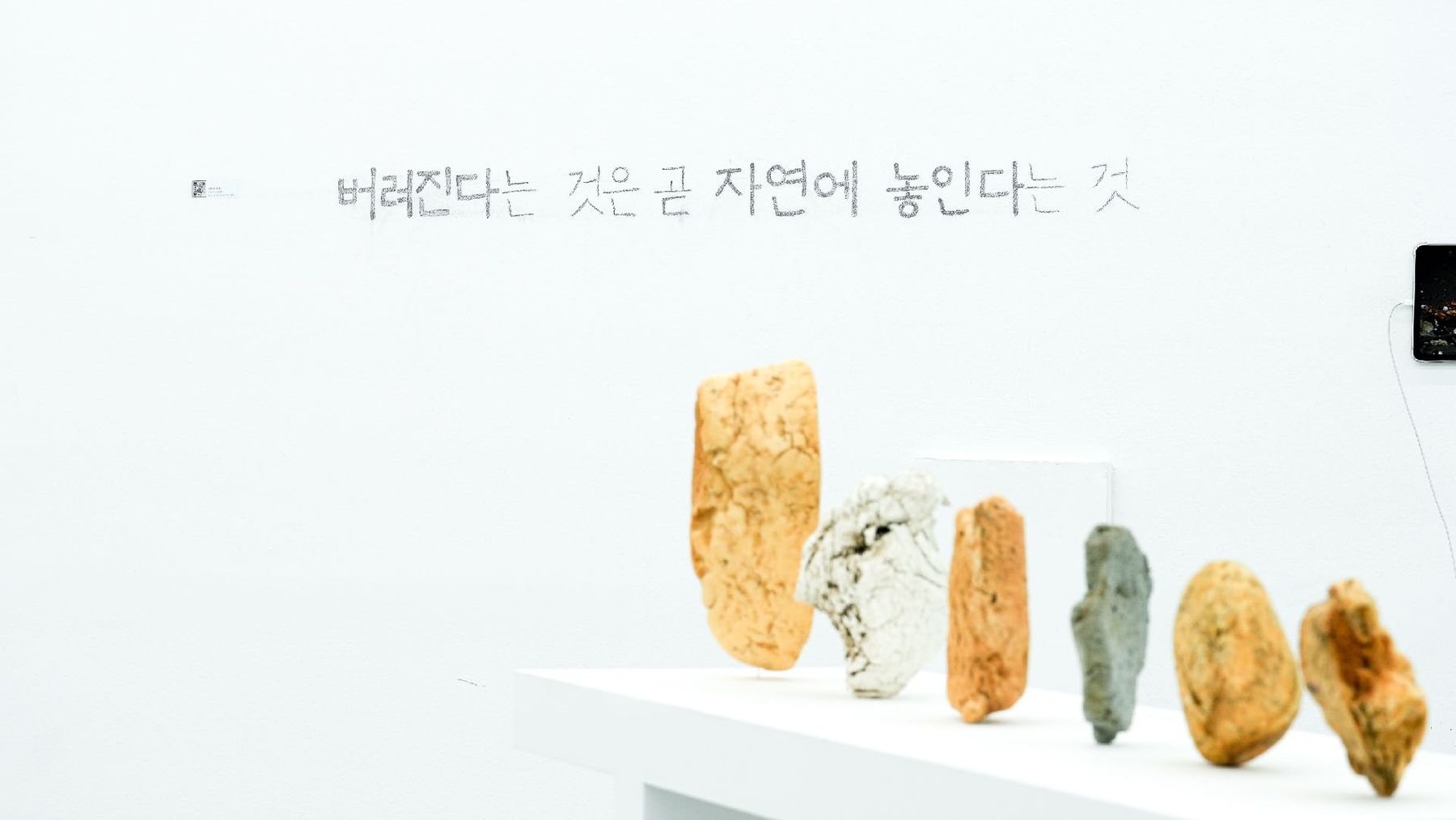 A long white gallery shelf holding a row of coloured New Rock specimens