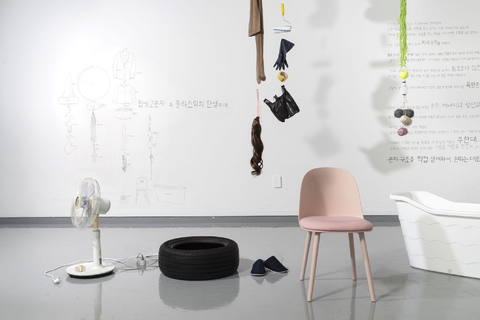 Gallery installation with hanging plastic objects, a chair, a bathtub and wall drawings