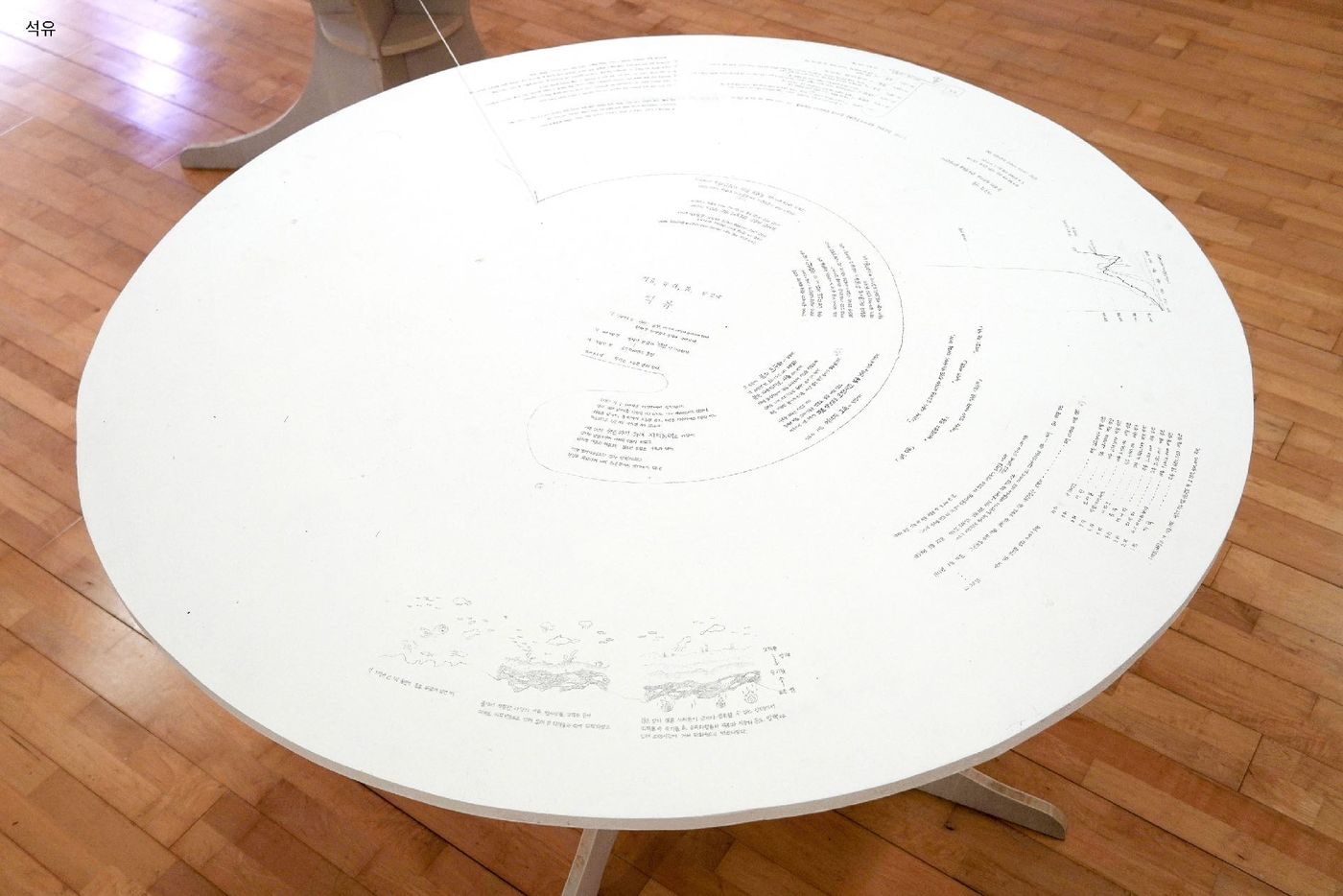 A large round white table covered in fine pencil drawings and text