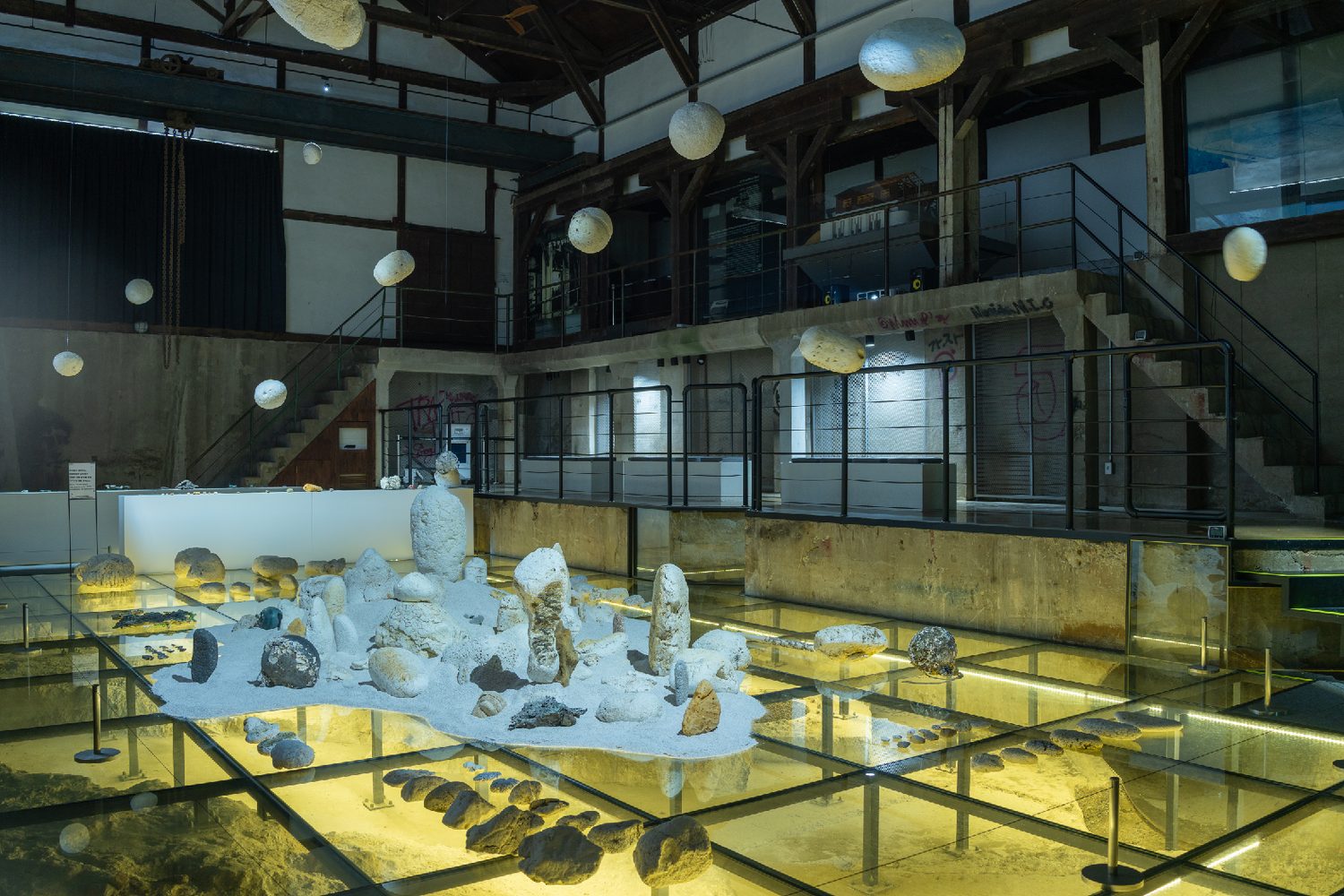 Pale blue plastic forms rising from a sand floor in a green-lit hall