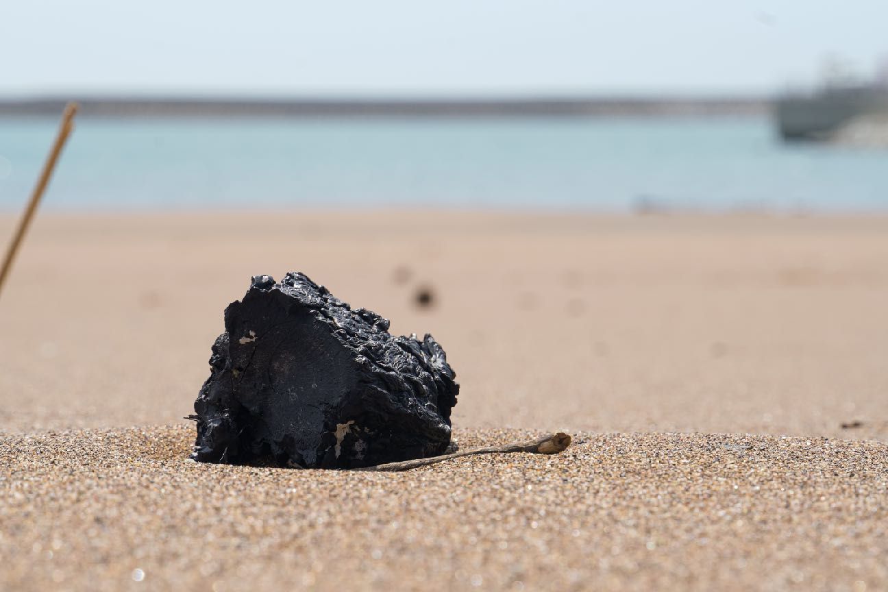 A small black weathered plastic form resting on pale beach sand