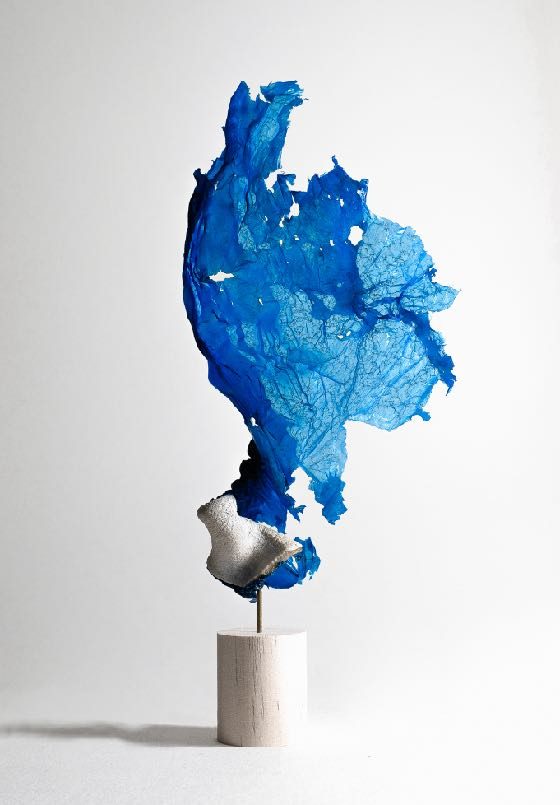 A vivid blue melted plastic form displayed upright on a small pedestal