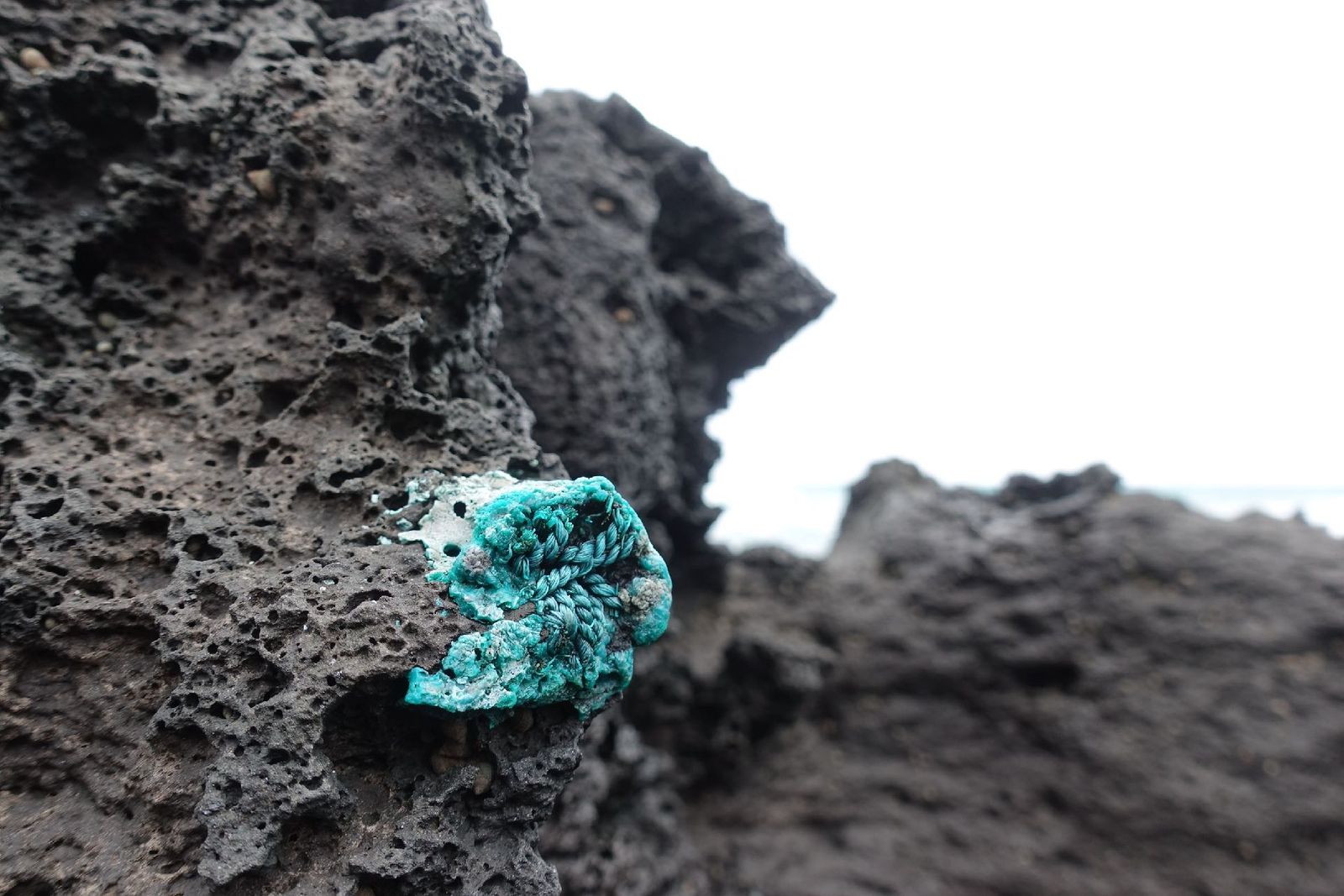 Turquoise melted plastic fused into black volcanic rock